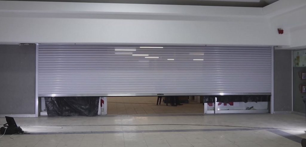 Wide light-grey commercial roller shutter door open inside a retail unit